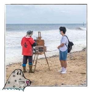 Image of an artist on the beach in Norfolk, UK, framed with a sketch line and overlaid with a hand drawn image of a seal