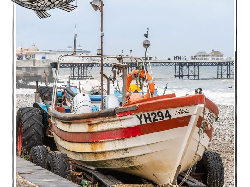 Image of a fishing boat on the beach in Norfolk, UK, framed with a sketch line and overlaid with a hand drawn image of a fish