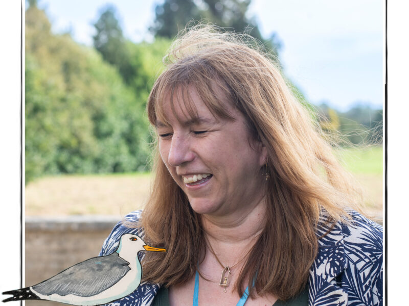 Image of a laughing woman against the background of fields and trees It is framed by a sketch line and overlaid with a hand drawn image of a standing seagull