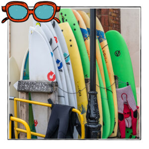Image of a rack of surfboards near the beach in Norfolk, UK, framed with a sketch line and overlaid with a hand drawn image of sunglasses
