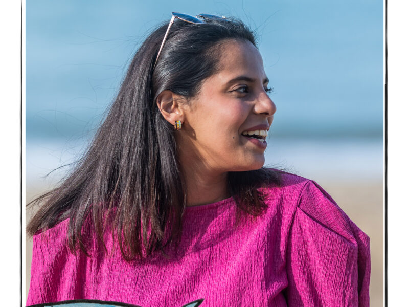 Image of a smiling woman in a bright pink top against the background of a beach. It is framed by a sketch line and overlaid with a hand drawn image of a fish