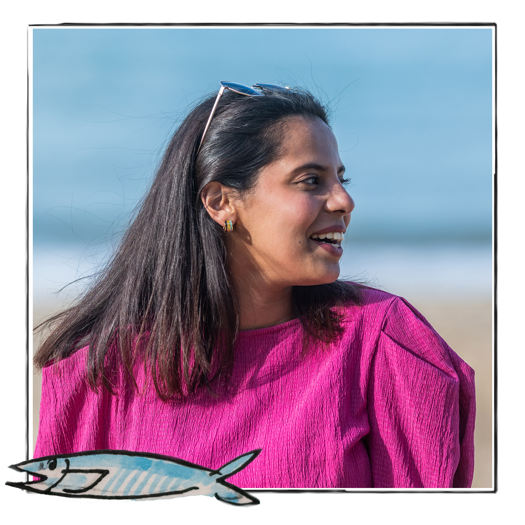 Image of a smiling woman in a bright pink top against the background of a beach. It is framed by a sketch line and overlaid with a hand drawn image of a fish