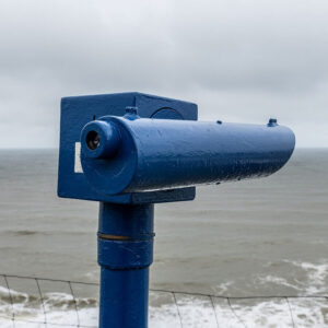 A telescope looking out at a gloomy sea in cromer signifying looking out at the outlook of AI SEO and Search. The telescope is blue, the sea is grey and the sky is cloudy.