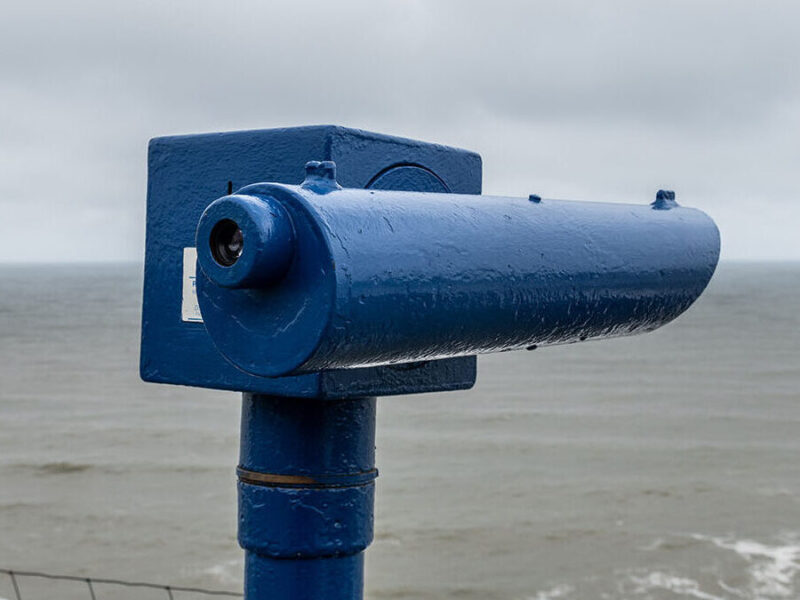 A telescope looking out at a gloomy sea in cromer signifying looking out at the outlook of AI SEO and Search. The telescope is blue, the sea is grey and the sky is cloudy.